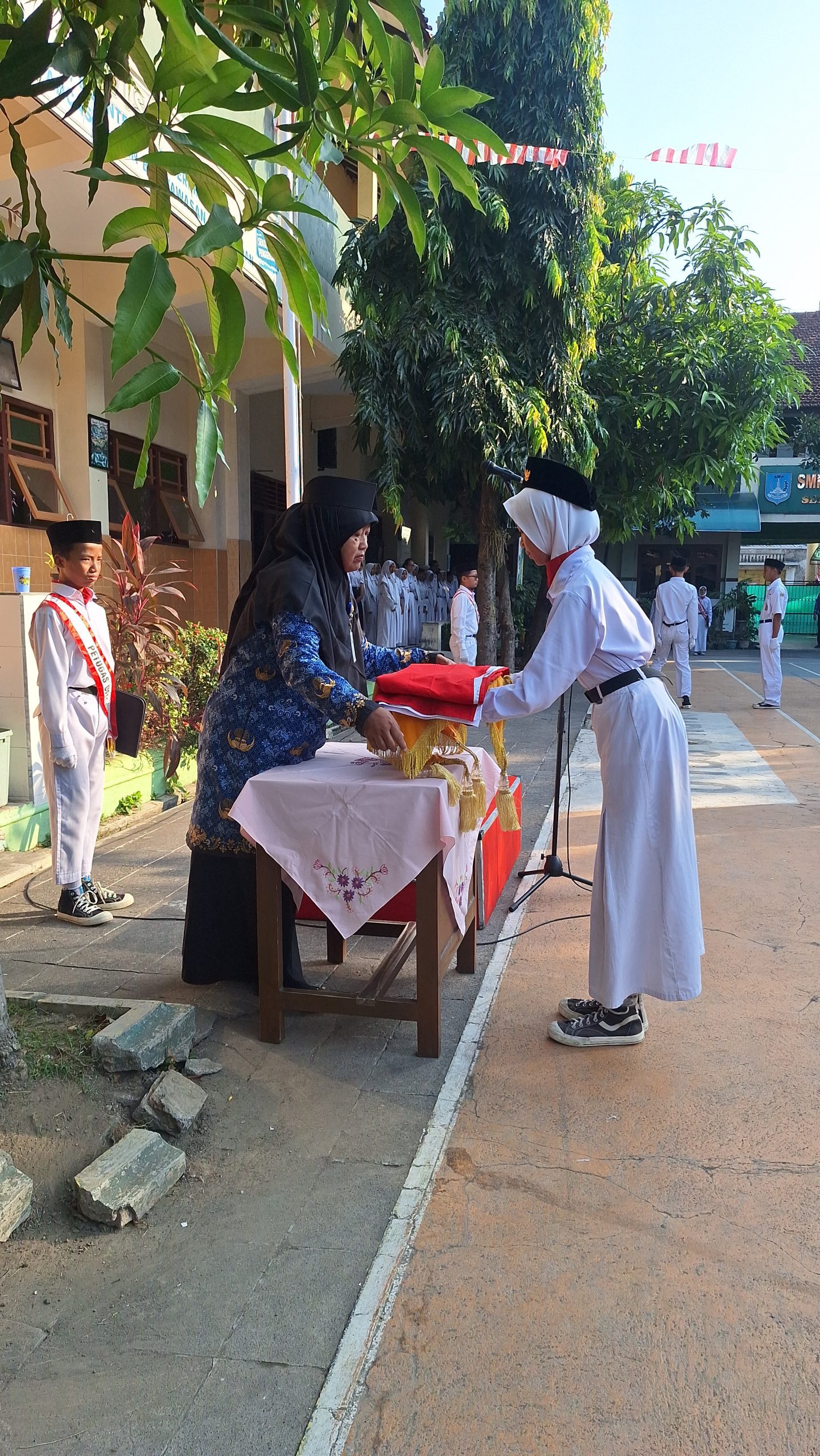Penyerahan bendera oleh pembina upacara, Sri Hastuti, S.H. kepada pembawa baki bendera, Khandra Lakeisha (IX E).